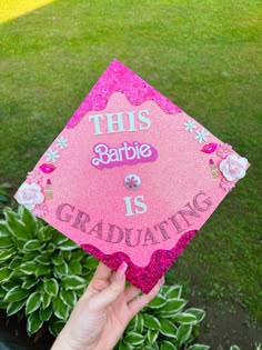 someone holding up a pink graduation cap that says, this barbie is graduating