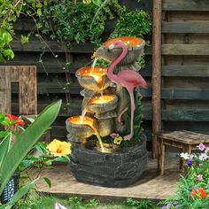 a fountain with flamingos and other plants surrounding it in a garden area, surrounded by wooden pallets