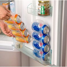 a person reaching into an open refrigerator to grab cans of soda from the fridge door