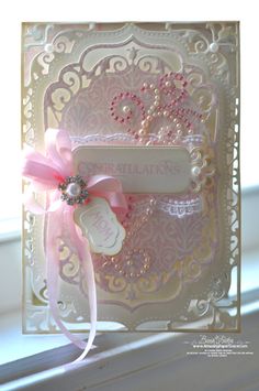 an ornate card with pink ribbon and pearls on it, sitting on a window sill