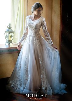 a woman in a wedding dress standing by a window