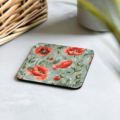 a square coaster with an image of red poppies on a blue background, next to a wicker basket