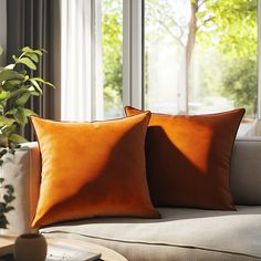 two orange pillows sitting on top of a couch in front of a window with trees outside