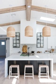 an open kitchen with two stools in front of the island and three pendant lights hanging from the ceiling