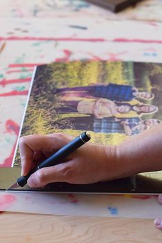 a person's hand holding a pen and writing on a piece of art paper