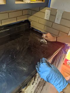 a man in blue gloves painting a kitchen counter with black paint on the top and bottom