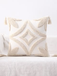 a white pillow with tassels on it sitting on top of a couch next to a blanket