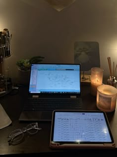 two laptops sitting on top of a desk next to a candle and some glasses