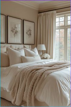 a bed with white sheets and pillows in front of two framed pictures on the wall