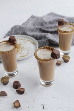 three small glasses filled with chocolate drink on top of a white table next to a plate