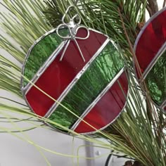 two stained glass ornaments hanging from a pine tree with green and red stripes on them