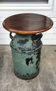 an old green bucket with a wooden table top on it's lid sitting in front of a white door