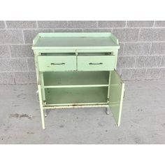 an old green metal cabinet with two drawers on it's legs and one drawer open