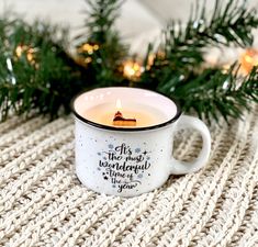 a white coffee cup with a candle in it on top of a knitted blanket