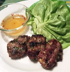 some meat patties and lettuce on a plate next to a bowl of dressing