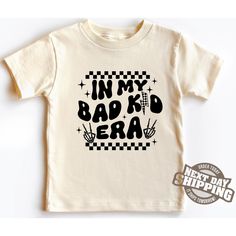 -In My Bad Kid Era Toddler T-Shirt - Trendy Black and White Funny Kids Tee, Cool Graphic Shirt, Edgy Toddler Outfit, Baby Boy Girl Gift Welcome to LittleLambsLounge! Fabric Information: -100% Cotton T-Shirts -Made to order -Handmade, unique designs -Ships the next business day -Our products come in 3 types: onesie® bodysuit, toddler, and youth size shirt. -The monthly sizes you choose will come as bodysuit® onesie®, available in both long sleeve and short sleeve options. We take pride in offering a delightful range of clothing for your little ones, crafted from super-soft fabrics that both you and your baby will adore. Our commitment is evident in every thread, as each piece is sustainably handmade-to-order, accompanied by a certificate of authenticity. FEATURES: We prioritize your kids' c Kids Funny T Shirts, Funny Kids Tee Shirts, Playful Funny Print T-shirt For First Birthday, Funny Toddler Shirts Svg, Innapropriate Kids Shirts, Kids Shirts Design, Bad Kids, Long Sleeve And Shorts, Kid Tees