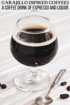 a glass of coffee sitting on top of a table next to spoons and beans