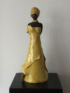 a yellow ceramic figurine sitting on top of a black table next to a white wall