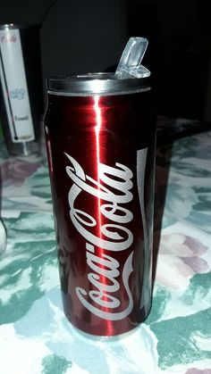 a coca - cola can sitting on top of a table next to a cup with a straw in it