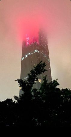 the top of a tall building is lit up with red lights and fog in the sky