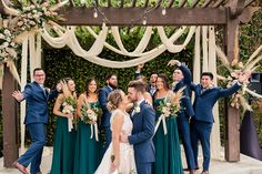 a group of people standing next to each other in front of a wooden structure with flowers and greenery