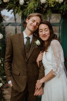 a man and woman standing next to each other in front of a green wall with flowers