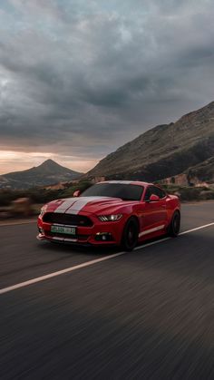 a red sports car driving down the road with mountains in the background