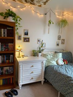 a bedroom with a bed, book shelf and bookshelf in the corner is lit by fairy lights