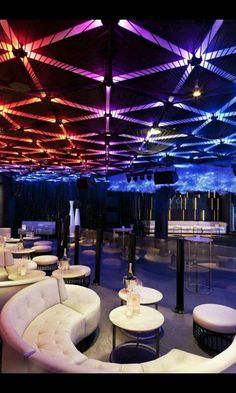 a large room filled with white couches and tables covered in colorful light beams above them