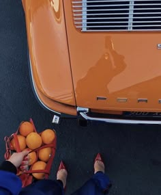 an orange car parked next to a woman with her feet on some oranges in front of it