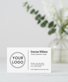 a white business card sitting on top of a table next to a vase with flowers