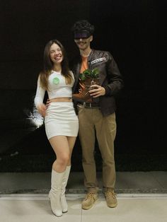 a man and woman standing next to each other in front of a black wall holding plants