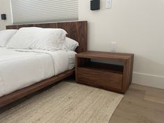 a bed with white sheets and pillows next to a night stand on a wooden floor