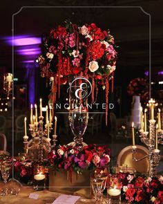 a table topped with lots of red and pink flowers next to tall candelabra filled with candles