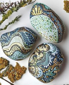 three painted rocks sitting on top of a white surface next to dried herbs and twigs