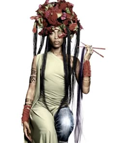 a woman with flowers on her head and long hair holding two sticks in one hand