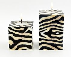 two zebra print candles sitting next to each other on a white surface with one candle lit in the middle