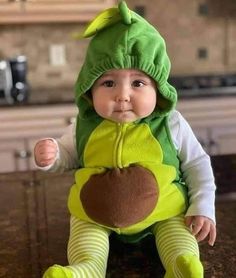 a baby sitting on top of a counter wearing a frog costume