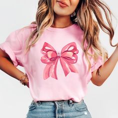 Embrace elegance and flirtatious charm with our captivating pink bow shirt, a delightful addition to your coquette-inspired wardrobe! 🌸👚 This shirt embodies the essence of femininity and playfulness, perfect for those who adore a touch of chic sophistication with a hint of flirtation. 🌷 The darling pink hue complements the shirt's design, accentuating the focal point--an exquisitely crafted oversized bow adorning the neckline or sleeves, adding a whimsical and flirtatious allure to your ensem Feminine Pink Crew Neck T-shirt, Cute Bow T-shirt For Spring, Feminine Pink Summer Shirt, Feminine Pink Shirt For Summer, Feminine Party Tops With Bow Detail, Cute Pink T-shirt With Bow, Feminine Tops With Ribbon For Spring, Feminine Ribbon Tops For Spring, Pink Party Top With Bow