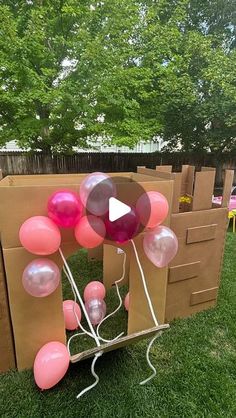 a bunch of balloons are in the grass near some cardboard boxes and tables with chairs