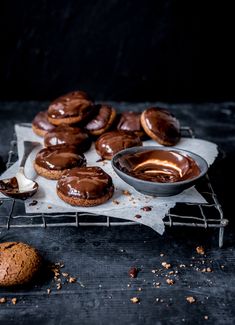 chocolate covered donuts on a cooling rack next to a bowl of frosted cookies