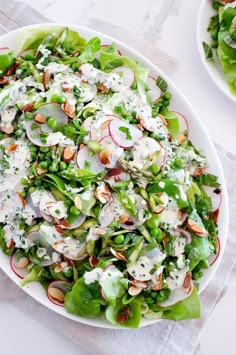 a salad with radishes, almonds and dressing in a white bowl on a table