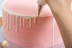 someone is decorating a pink cake with icing on the top and white drips