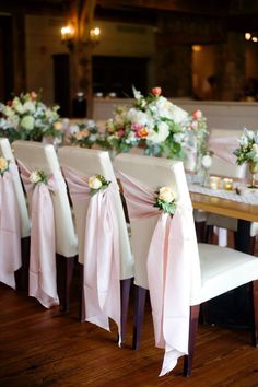 a row of chairs with pink sashes and flowers on them at a wedding reception