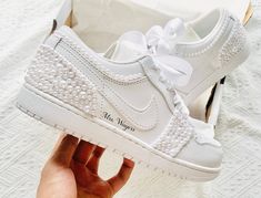 a person holding up a white nike air force 1 with pearls on the soles