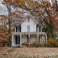 an old white house surrounded by trees and leaves