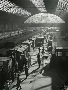 an old black and white photo of people at a train station with trains on the tracks