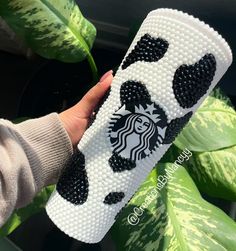 a hand holding a starbucks cup case with black and white designs on the bottom, in front of a green plant