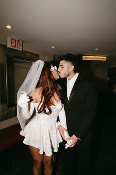 a bride and groom kissing in the hallway at their wedding reception with an exit sign behind them