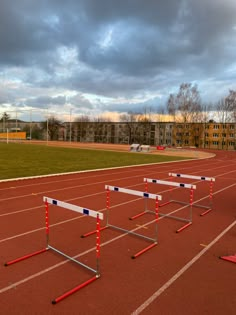 three hurdles in the middle of a track with buildings in the background and dark clouds overhead